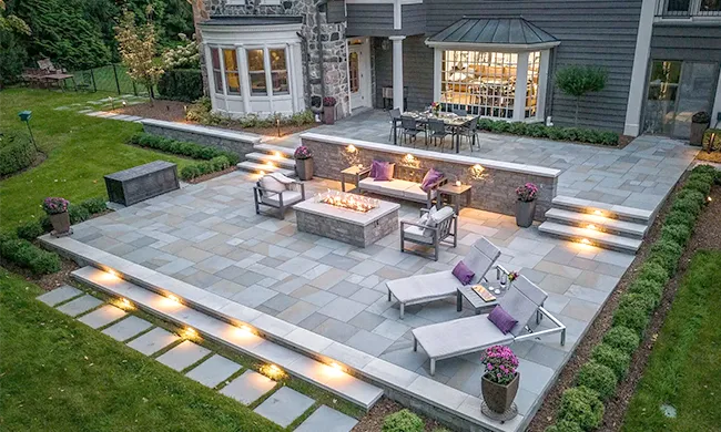 custom-hardscaping-stone-patio-fire-pit-worcester-ma.webp" alt="Custom stone paver patio featuring a built-in fire pit and retaining walls, installed in Worcester, MA